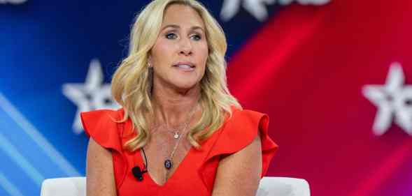 Marjorie Taylor Greene wears a red outfit as she sits on a while couch during a conference