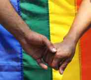 Two men holding hands in front of a pride flag.