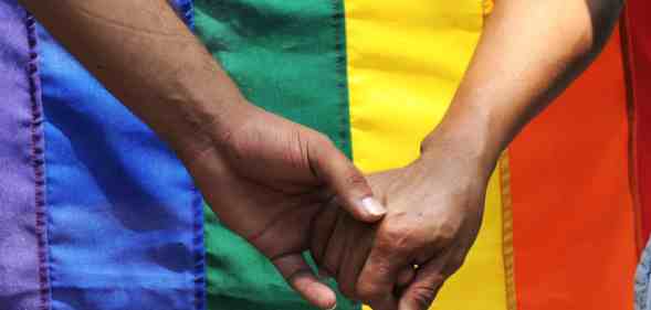 Two men holding hands in front of a pride flag.