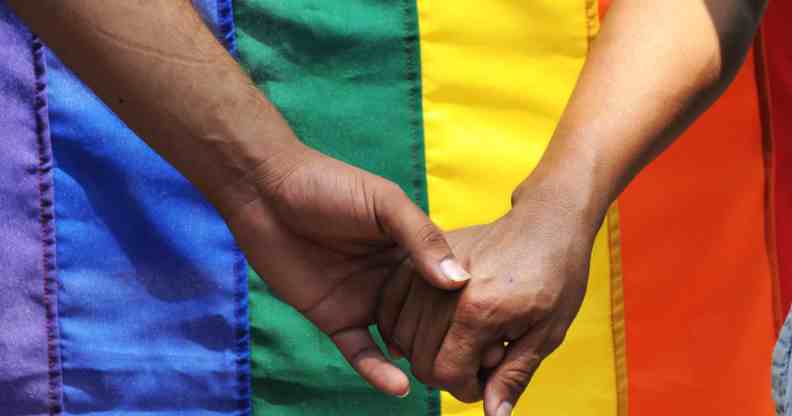 Two men holding hands in front of a pride flag.