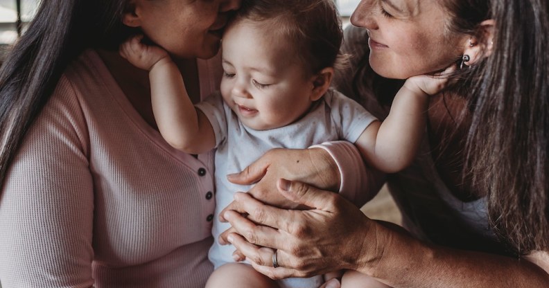 In this stock photo, two women hold a baby as it touches both of their faces