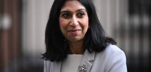 Suella Braverman wears an off-white blazer with a pin on top of a white outfit