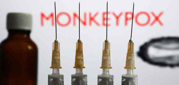 Medical syringes and a bottle are seen with 'Monkeypox' sign and monkeypox illustrative model displayed on a screen in the background in this illustration photo taken in Krakow, Poland.