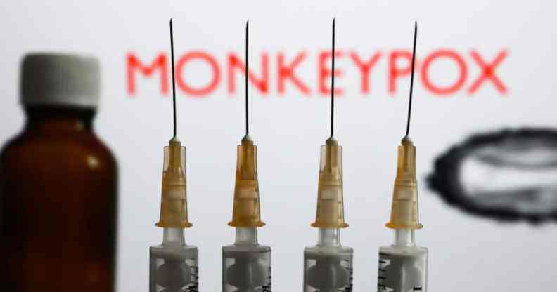 Medical syringes and a bottle are seen with 'Monkeypox' sign and monkeypox illustrative model displayed on a screen in the background in this illustration photo taken in Krakow, Poland.