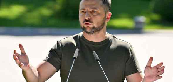 A photo shows Ukrainian President Volodymyr Zelensky wearing a dark green t-shirt as he speaks into two microphones