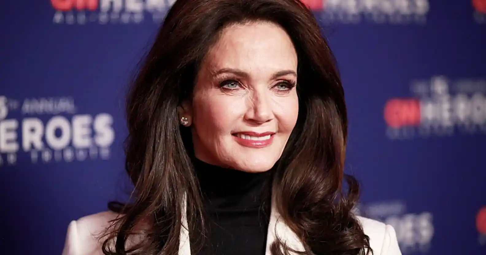 Lynda Carter wearing a grey suit and black turtleneck on a red carpet.