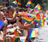 In this photograph, people wave rainbow Pride flags at a barrier