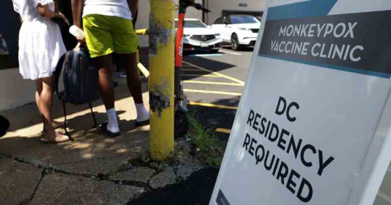 People wait in line for a monkeypox vaccine as a sign outside reads 'Monkeypox vaccine clinic DC residency required'