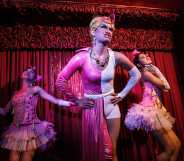 Three drag queens on a stage performing wearing pink dresses.