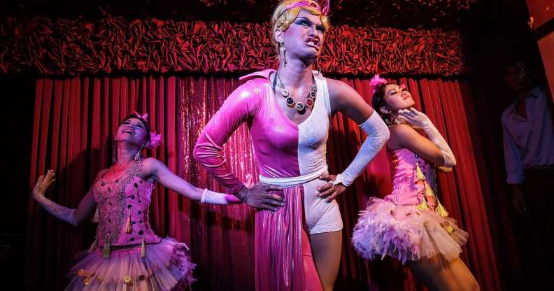 Three drag queens on a stage performing wearing pink dresses.