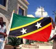 In this photograph, two men hold the St Kitts and Nevis Flag by a government building (Getty)