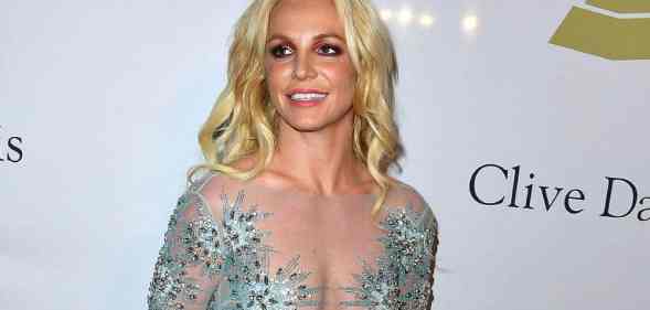 Britney Spears smiles at someone off camera while wearing a semi-transparent dress with blue crystal details on it