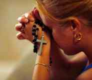 A young woman holding rosary beads in her hands prays