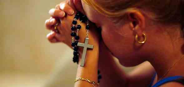 A young woman holding rosary beads in her hands prays