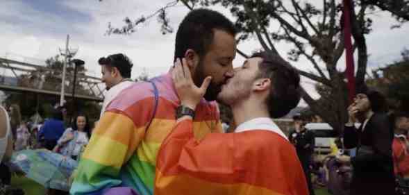 Two people wearing rainbow colours kiss in a park in Bogota, Columbia during a LGBTQ+ protest