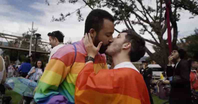 Two people wearing rainbow colours kiss in a park in Bogota, Columbia during a LGBTQ+ protest