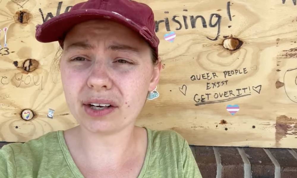 UpRising Bakery and Café owner Corrina Sac wears a light green shirt and red cap as she sits outside her business which has boards over the windows after the business was vandalised for planning to host a family-friendly drag event