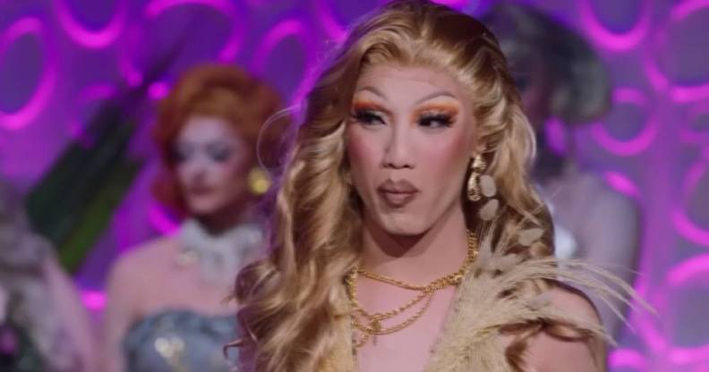 Drag Race Down Under season two queen Faúx Fúr looks off camera while wearing a cream outfit with other queens standing in the background