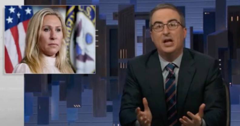 John Oliver wears a blue shirt, striped tie and dark suit jacket on the set of HBO Max's Last Week Tonight. There is an image of Georgia congresswoman Marjorie Taylor Greene in the corner. Greene is wearing a white top as she stands in front of a US flag