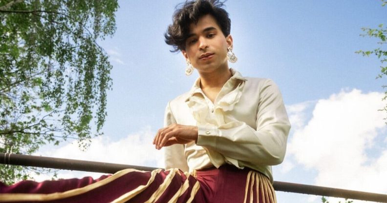 Shiva Raichandani in a white top and red and gold trousers leaning against a fence.