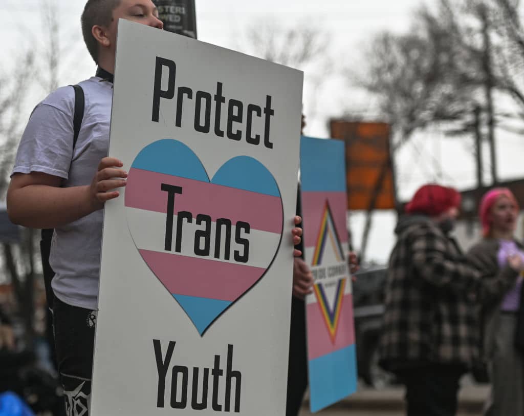 An activist holds a placard with words 'Protect Trans Youth'.