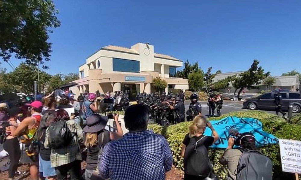 In this video screenshot, police circle protesters outside a building