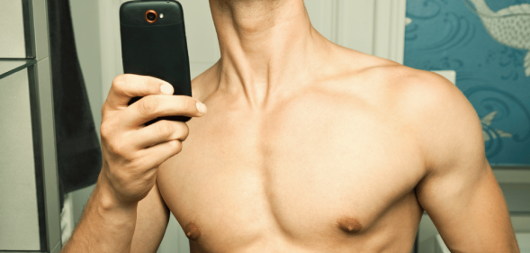 A topless man taking a mirror selfie, his face cropped out