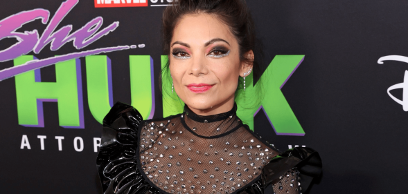 Ginger Gonzaga stands at the red carpet infront of a backdrop consisting of She-Hulk advertisements.