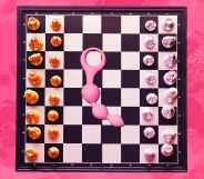 An image of a chess board against a pink background with anal beads in the centre of the board.