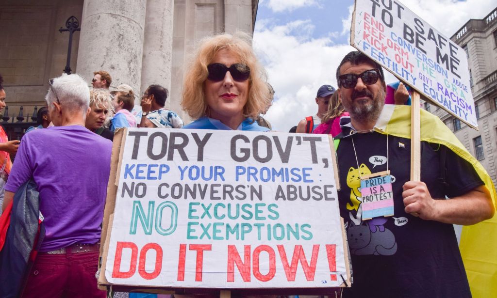 Two people hold up signs calling on the UK government to ban conversion practices