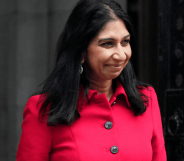 Suella Braverman wears a pink-red outfit as she smiles at someone off camera