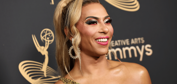 Shangela wears a gold dress as she stares somewhere off camera