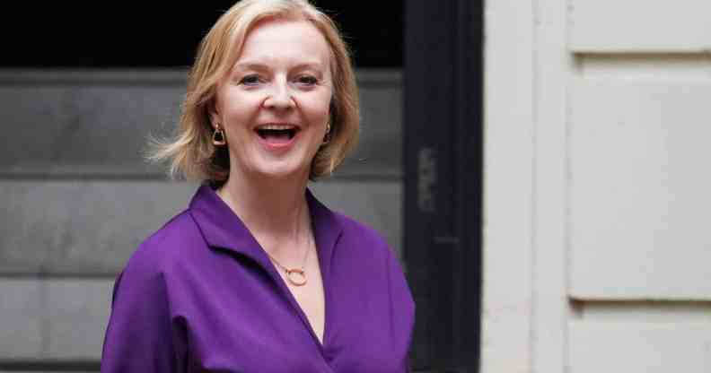 Liz Truss smiles as she stands outside a building wearing a purple outfit