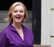 Liz Truss smiles as she stands outside a building wearing a purple outfit