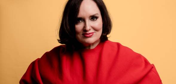 A publicity photo showing comedian Deborah Frances-White from The Guilty Feminist, wearing a red outfit
