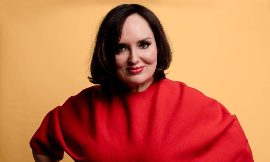 A publicity photo showing comedian Deborah Frances-White from The Guilty Feminist, wearing a red outfit