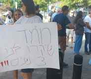 A parent stands outside the demonstration area holding a sign in hebrew.