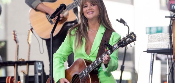 Maren Morris in a green suit playing the guitar.