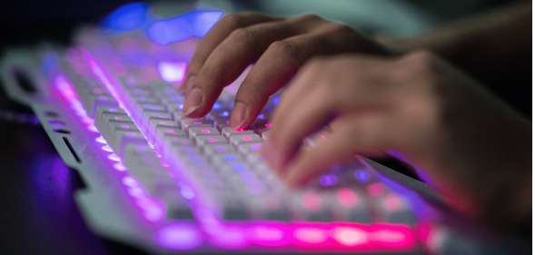 A person types on a white keyboard with LEDs lighting it up.