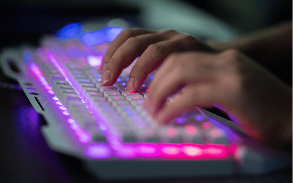 A person types on a white keyboard with LEDs lighting it up.