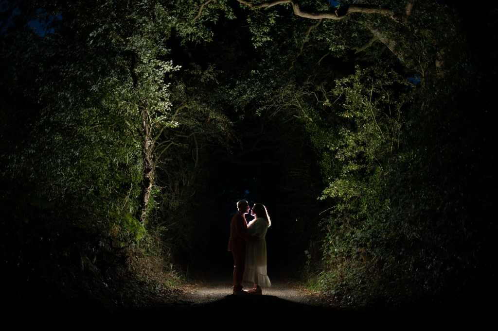 A wide shot of Tom and Amy embracing in the dark, with trees lit up around them