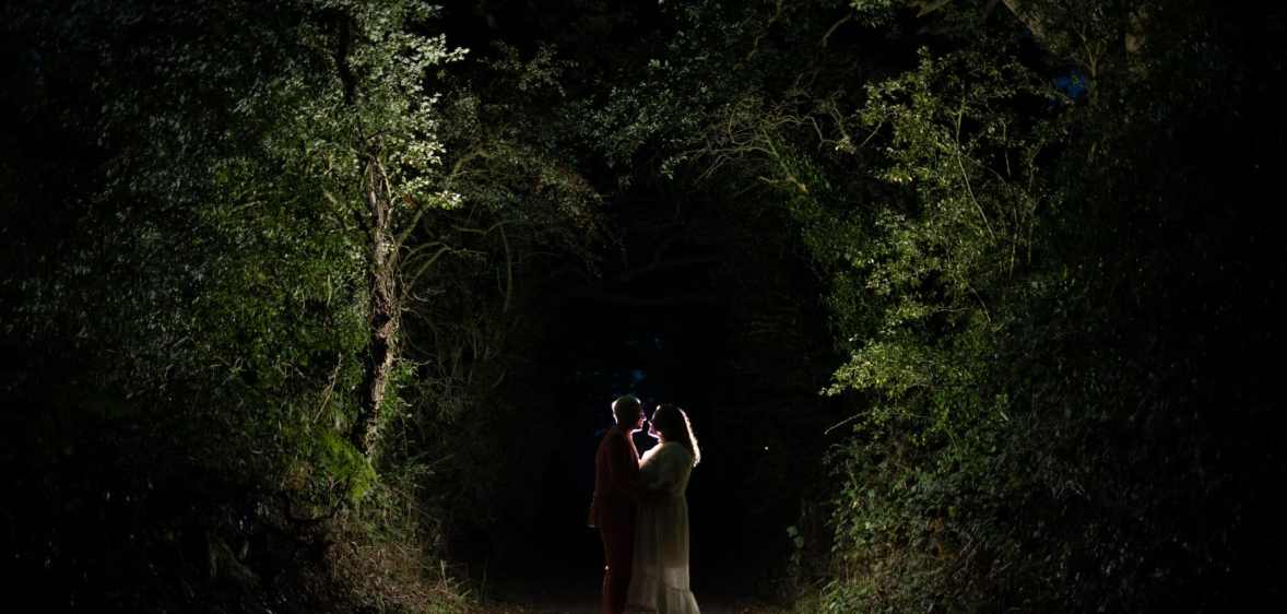 A wide shot of Tom and Amy embracing in the dark, with trees lit up around them