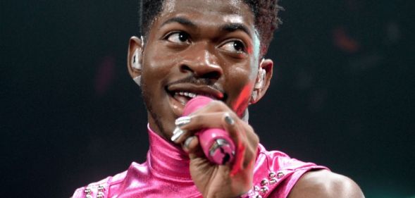 Lil Nas X wears a pink outfit as he sings into a microphone during a performance