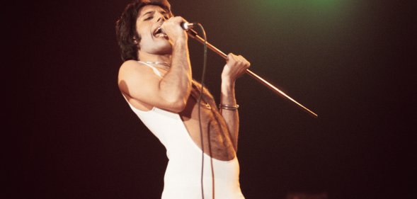 Freddie Mercury wears a white outfit as he sings on stage during a performance with the band Queen