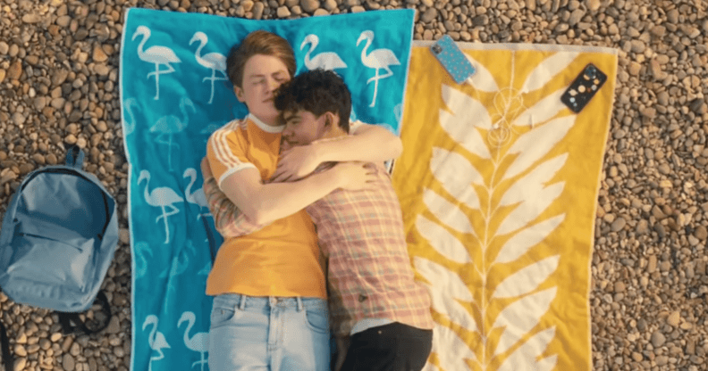 Heartstopper characters Nick and Charlie hold each other as they enjoy a day at the beach in an episode of the Netflix series