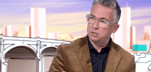 Iain Anderson wears a black shirt and brown jacket as he does an interview with Laura Kuenssberg on the BBC