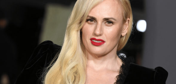 Rebel Wilson wears a black dress with her blonde hair styled over one shoulder