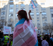 A person wears a trans Pride flag and waves a matching flag in their hand during a protest