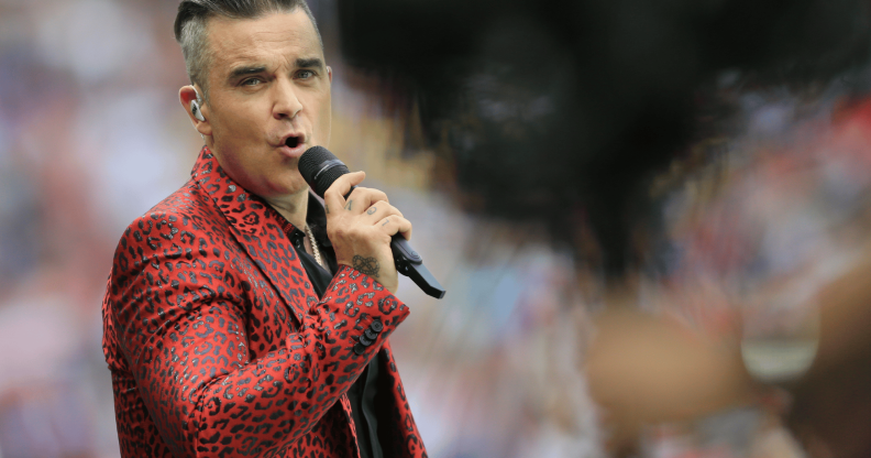 Robbie Williams wears a red animal-print patterned outfit as he sings into a microphone