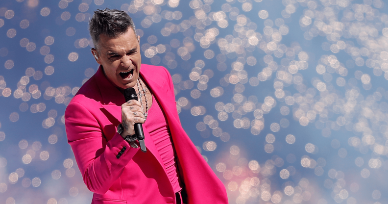Robbie Williams wears a pink outfit as he sings into a microphone